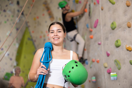 young positive muscular girl with necessary equipment stands in gym near climbing wallの写真素材