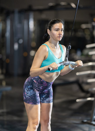 In gym, woman uses cable row machine to strengthen muscles.