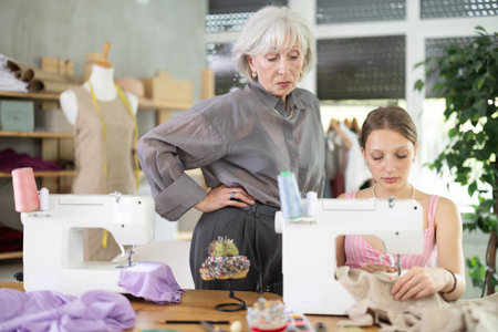 Elderly woman seamstress teaches young woman to sewの写真素材