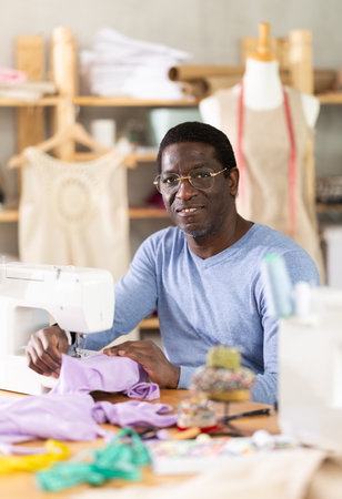 Working in sewing workshop - male tailor working at sewing machine making stitches on fabricの写真素材