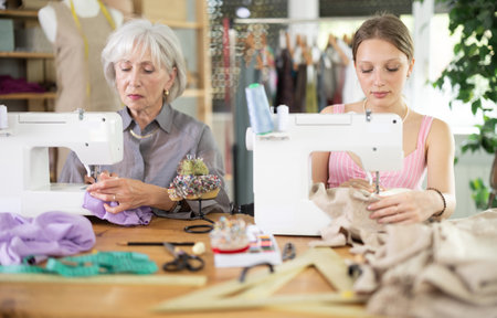 Elderly and young women seamstresses sewing on machineの写真素材