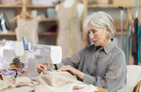 Woman seamstress sews on sewing machine in workshopの写真素材