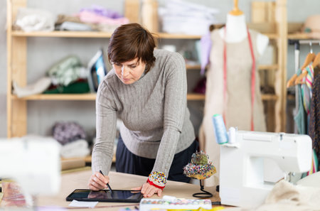 Woman tailor creates sketch of dress on tablet