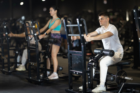 In gym, guy uses gym apparatus to strengthen back and shoulder musclesの写真素材