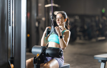Fit woman performing lat pulldown on cable machine at gym