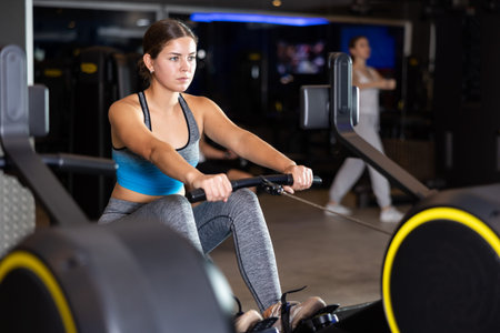 Sportive young girl training on cable row machine in gym