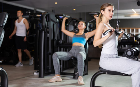 Sportive young girl training on lat pull down machine in gym