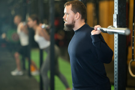 Determined young guy working out with weight rod during crossfit workout