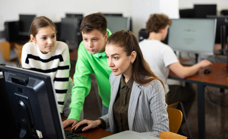 Female teacher and teenager pupils looking at monitor of PC