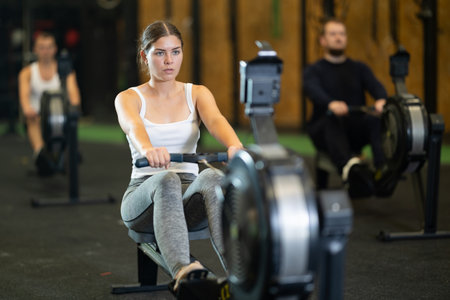 Girl exercising on rowing machine during intense full body workoutの写真素材