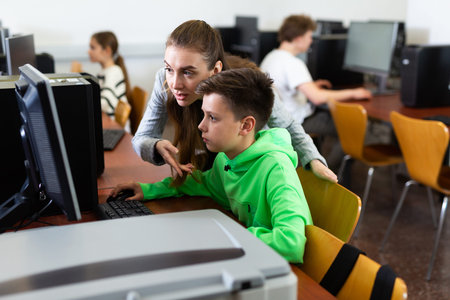 Female teacher consulting tween boy studying in computer class