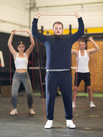 Motivated bearded guy doing exercises with elastic loop band in gym