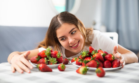 Portrait of a happy woman with strawberries at the table in room at homeの写真素材