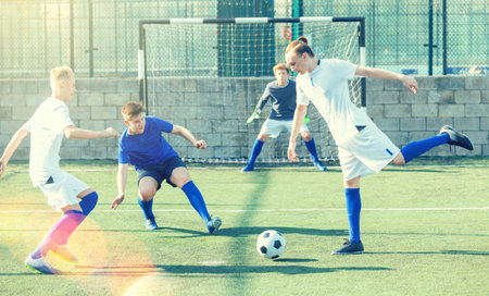 Game of football match between two teams of teenagers in white and blue shirtsの写真素材