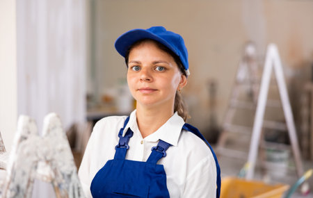 Portrait of contented young female builder in blue overalls during the repair of cottage