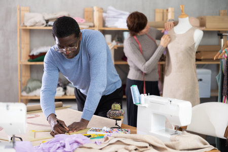 Male tailor draws sketch of future clothing on paper using patterns in sewing workshop