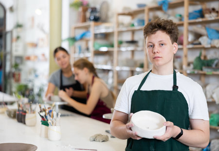 Boy teenager posing with ceramic bowl in ceramic workshopの写真素材
