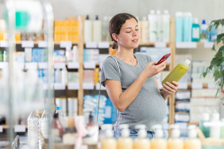 Young pregnant woman buyer scanning qr code for shampoo or shower gel in pharmacy shopの写真素材