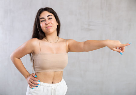 Young woman pointing aside standing against the wallの写真素材