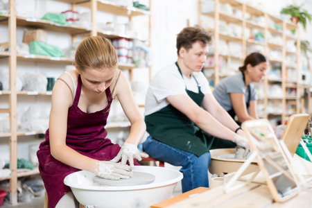 Young girl creates clay product on potter wheel in workshop