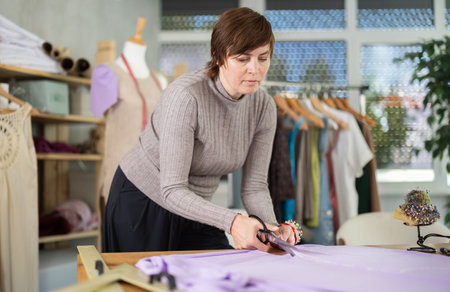 Woman seamstress cuts fabric on cutting table