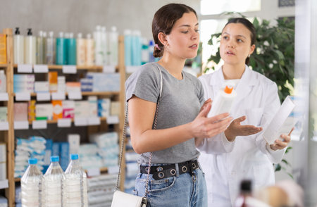 Young woman choosing cream while pharmacist offering in drugstoreの写真素材