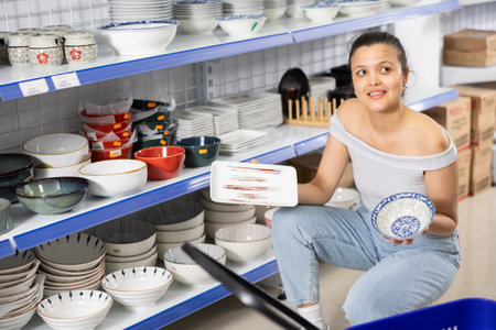 Woman looking for new plates at store of household goodsの写真素材