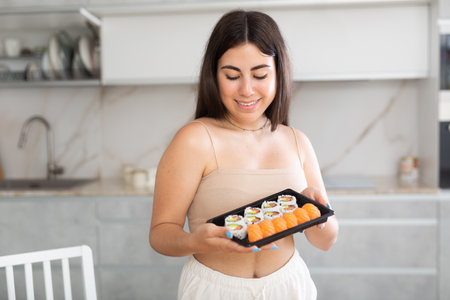 Smiling young woman holding sushi in the kitchenの写真素材