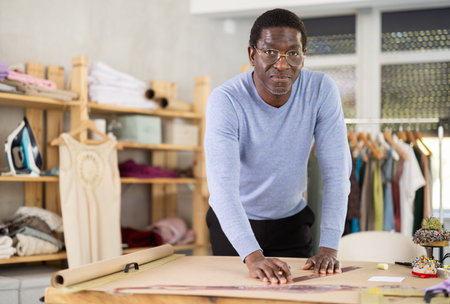 Male tailor draws sketch of future clothing on paper using patterns in sewing workshopの写真素材