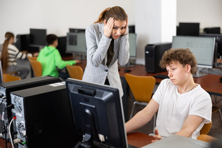 Frustrated teacher talking to neglectful teenage student in computer class
