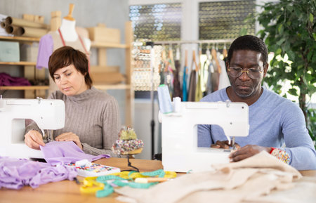Working in sewing workshop - man and woman working at sewing machines, creating new clothesの写真素材
