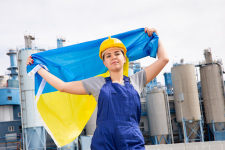 Happy woman waving flag of Ukraine against the background of modern factoryの写真素材