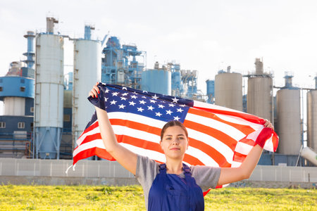 Calm young woman worker with flag of the USA against background of factory