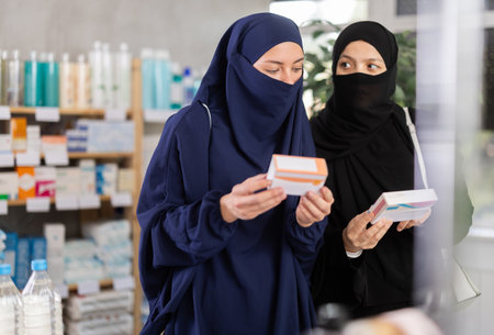 Two Muslim women choosing pills in box in drugstoreの写真素材