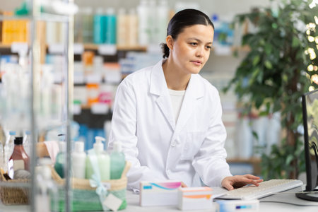 Female pharmacist updating stock inventory on pharmacy computerの写真素材