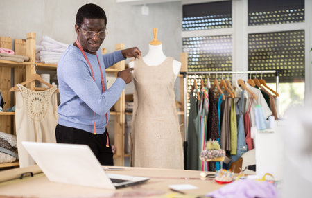 Male tailor sews new dress on a mannequin in sewing studioの写真素材
