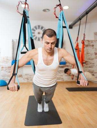 Man performing chest press with TRX straps during Pilates training
