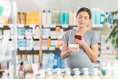 Positive pregnant woman choosing box with pills to improve well-being in pharmacy, scan QR code on labelの写真素材