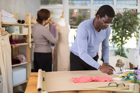 Male fashion designer drafting clothing pattern in studio with female colleague