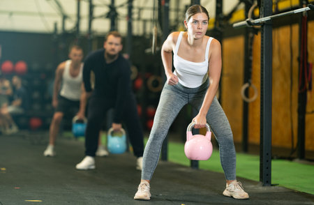 Fit girl doing exercises with kettlebell during group workoutの写真素材
