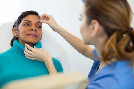 Cosmetologist touching face of Latin woman during examinationの写真素材