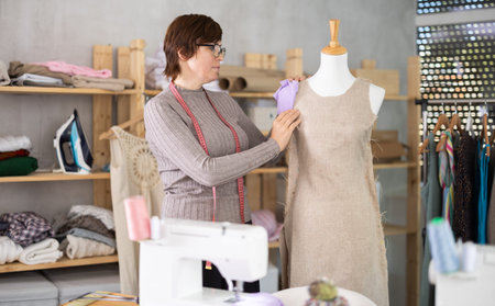 Female dressmaker trying on a new dress on a mannequin in sewing workshop