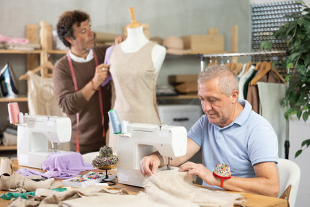 Mature man tailor at work, other man work with mannequin in backgroundの写真素材