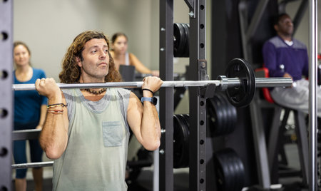 Caucasian sportsman doing squats with weight near squat rack in gym