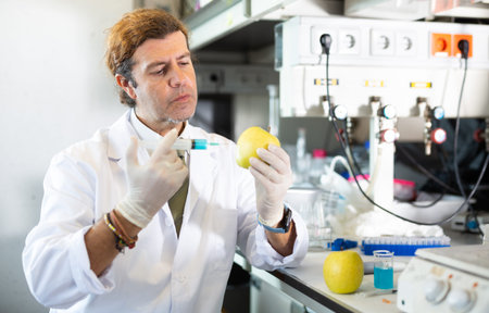 Scientist working in laboratory, injecting additives into fruit during experiments with genetically...