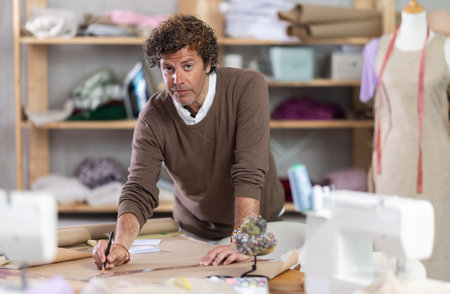 Man dressmaker drawing pattern on paper in workshop