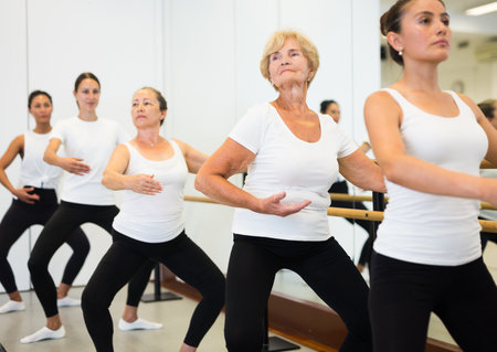 Elderly woman doing ballet steps at ballet barre in dance studioの写真素材