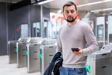 Guy traveler standing on subway station with phone in hands