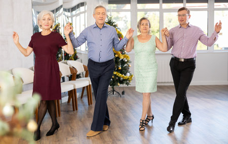 Group of elderly people with middle-aged man perform folk dance during New Year party