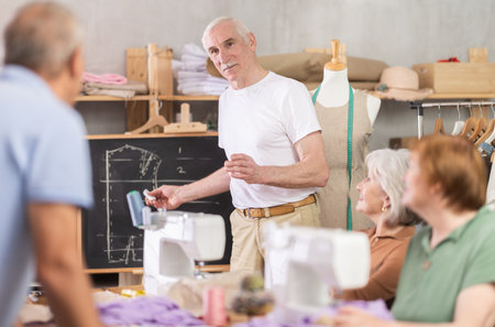 Aged teacher explaining pattern structure by chalkboard during sewing course for seniorsの写真素材